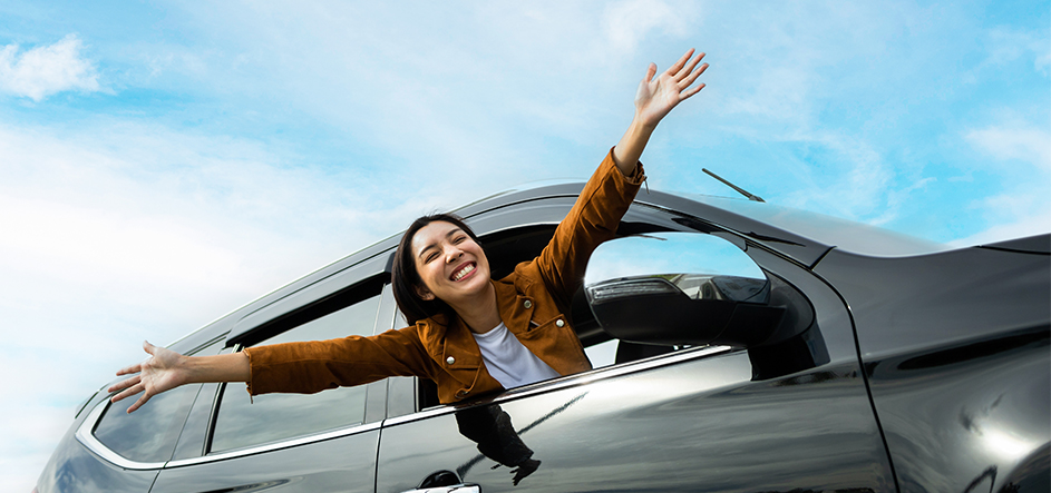 woman out passenger side car window smiling with hands raised