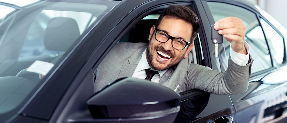 Man in the driver's seat of a vehicle smiling and holding up the keys to a new car.